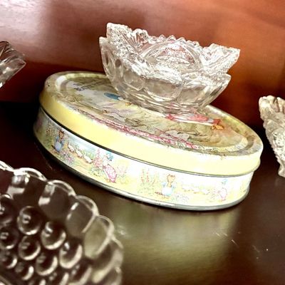 Sale Photo Thumbnail #101: Collection of vintage pressed and cut glass bowls, including a small footed dish resting on a decorative Beatrix Potter tin.