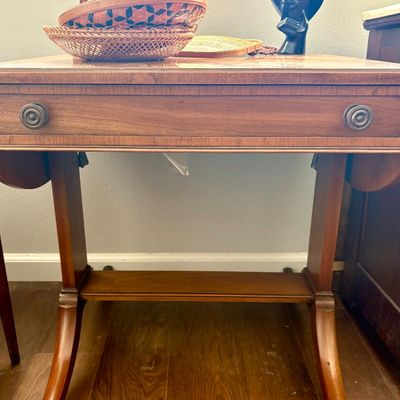 Sale Photo Thumbnail #96: Duncan Phyfe style mahogany drop-leaf table featuring a single drawer with brass pulls, splayed legs on casters, and a lower stretcher shelf.
