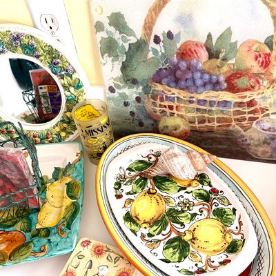Sale Photo Thumbnail #91: Assorted kitchen decor, including Italian-style ceramic lemon platters, a fruit basket cutting board, a majolica-style round mirror, and a wire napkin holder.