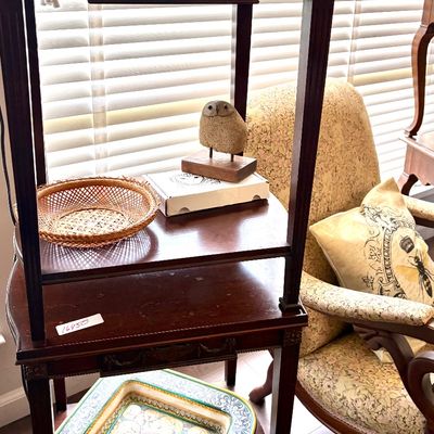 Sale Photo Thumbnail #98: Two stacked dark wood side tables featuring carved details, displaying a small woven basket, a decorative owl figurine, and a large patterned ceramic platter.