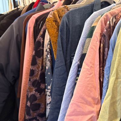 Sale Photo Thumbnail #61: Assorted clothing items, including shirts, jackets, and patterned tops, hanging on a rack.