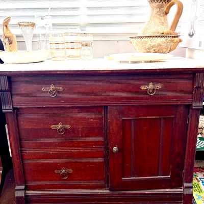 Sale Photo Thumbnail #86: Antique Eastlake-style mahogany washstand with a white marble top, featuring three drawers with brass ring pulls and a single cabinet door.