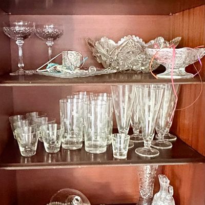 Sale Photo Thumbnail #84: Collection of vintage cut glass and crystal tableware, including bowls, tumblers, stemware, and serving dishes, displayed on wooden shelves.