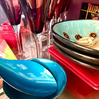 Assorted colorful tableware including turquoise ceramic bowls, red square plates, and tall ruby red wine glasses.