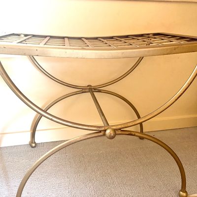 Hollywood Regency style gold-painted metal vanity bench featuring a curved, slatted seat and elegant X-frame base.