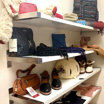 Assorted women's accessories and apparel displayed on floating shelves, including a Baggallini handbag, leather shoes, lace...