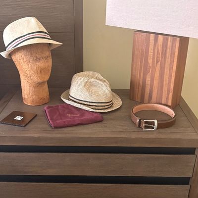 Modern three-drawer nightstand in a dark wood finish, styled with a wooden block table lamp, two straw fedora hats, a wooden mannequin...