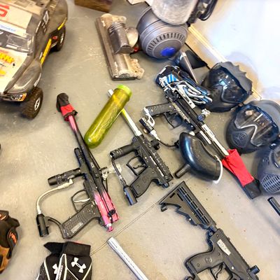 Collection of paintball gear including multiple markers, protective masks, a hopper, and accessories, alongside an RC truck and a Dyson...