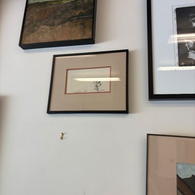 Collection of framed wall art, including a landscape painting, a small sketch of a dog, and other matted prints in black frames.
