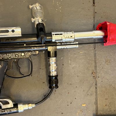 Vintage mechanical paintball marker featuring a black body, silver accents, and a red barrel sleeve.