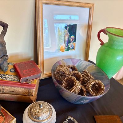 Assorted vintage decor items including a green glass vase with red handles, a bowl of beaded napkin rings, a small framed artwork, and a...