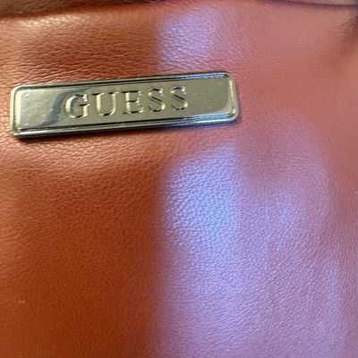 Close-up of a Guess brand logo plate on a brown faux-leather bag.