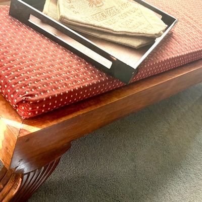 Mid-century modern style wooden bench with a red and white patterned cushion, featuring a black serving tray with burlap napkins on top.