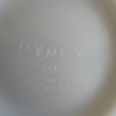 Close-up of the embossed Pyrex maker's mark on the bottom of a white milk glass dish, reading "Pyrex Made in U.S.A....