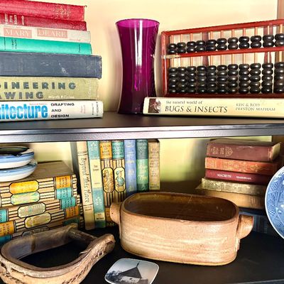 Assorted vintage collectibles on wooden shelves, including a wooden abacus, a purple glass vase, various vintage books, a 1980...