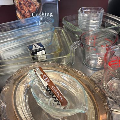 Assorted kitchenware including Pyrex glass baking dishes, measuring cups, a Clos Du Val corkscrew, and silver-plated serving trays.