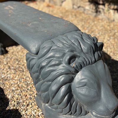 Concrete garden bench featuring sculpted lion head supports, finished in a dark gray paint.