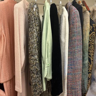 Assortment of vintage women's clothing hanging on a rack, featuring textured blazers, a sequined jacket, and a plush faux fur coat.