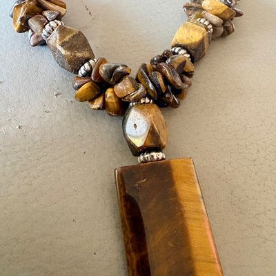 Tiger's eye statement necklace featuring a large rectangular pendant, faceted accent beads, and polished chips on a brown cord.