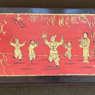 Vintage Chinese lacquer box lid featuring a hand-painted scene of figures in gold on a red background, framed by a dark border.