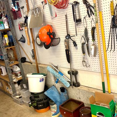 Assorted garage and garden tools, including a pegboard organizer with hand tools, extension cords, a safety helmet, long-handled garden...