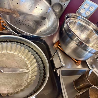 Assorted vintage and modern kitchenware, including stainless steel mixing bowls, a colander, tart pans, baking sheets, and knives,...
