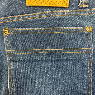 Nasty Pig Incorporated blue jeans, featuring a back pocket with orange stitching, metal grommets, and a branded leather waist patch.