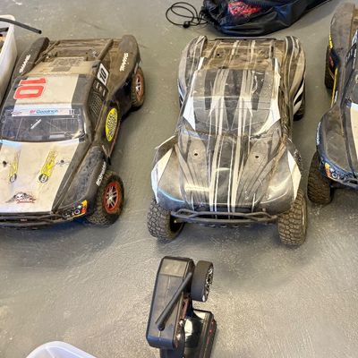 Three Traxxas RC short course trucks with controllers and accessories, showing signs of use.