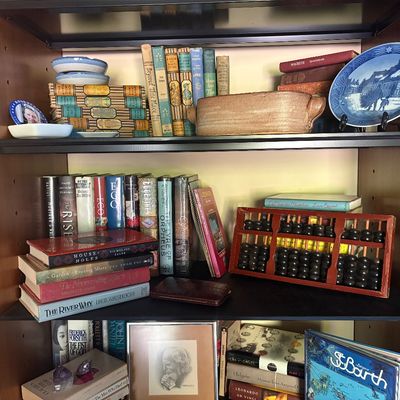 Wooden bookshelf filled with vintage books, a wooden abacus, decorative plates, and various small collectibles.