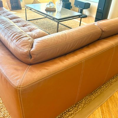 Contemporary tan leather sectional sofa featuring tufted seat cushions and contrast stitching, shown in a living room setting.