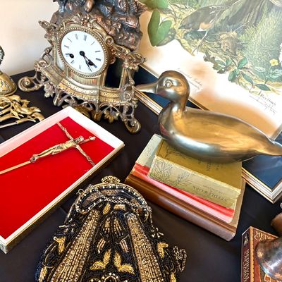Assortment of vintage collectibles including an ornate brass mantel clock, a brass duck figurine, a beaded evening bag, and a crucifix...