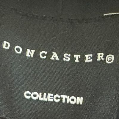 A black woven brand label for "Doncaster Collection" sewn onto a dark garment.