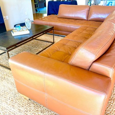 Contemporary tan leather sectional sofa with tufted seat cushions, paired with a dark metal frame coffee table on a woven area rug.