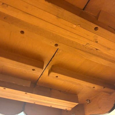 Underside view of a vintage wooden dining table, showing the extension slide mechanism and solid wood construction.