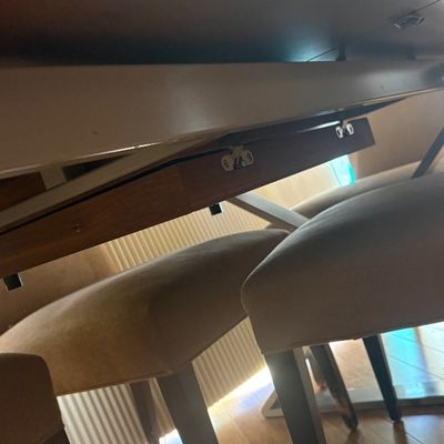 Underside view of a modern dining table with a metal support frame, shown alongside upholstered dining chairs.