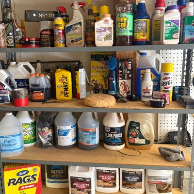 Assorted household, automotive, and garden chemicals on a four-tier metal shelving unit, including cleaners, sealers, and lubricants.