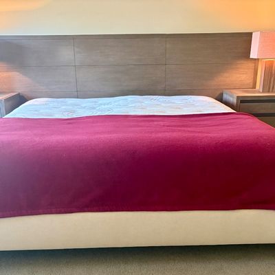 Modern king-size bedroom set featuring a wide, paneled wood headboard, two matching three-drawer nightstands, and a pair of block-style...