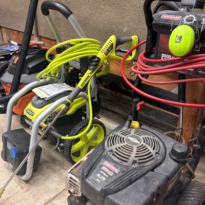Ryobi electric pressure washer and a Craftsman gas-powered pressure washer, shown with hoses and accessories in a garage setting.