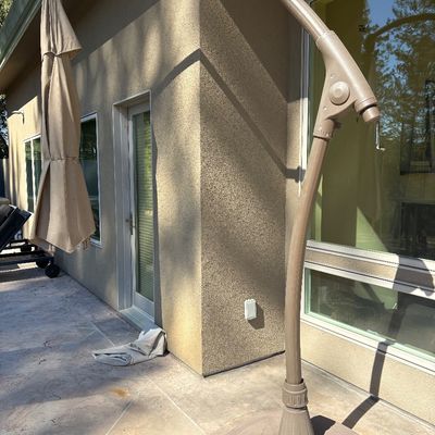 Large cantilever patio umbrella with a beige fabric canopy, curved metal frame, and a heavy molded base.