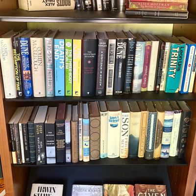 A collection of hardcover and paperback fiction books, including titles by Frank Herbert, Ken Follett, and Stieg Larsson, arranged on a...