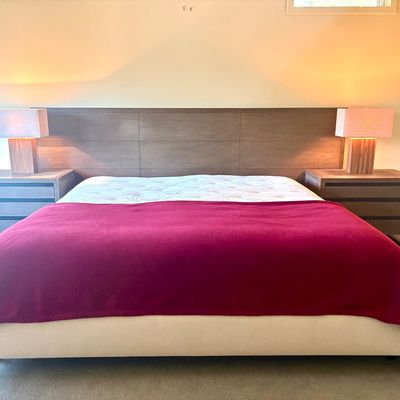Contemporary king-size platform bed featuring a wide, paneled wood headboard, matching three-drawer nightstands, and a pair of modern...