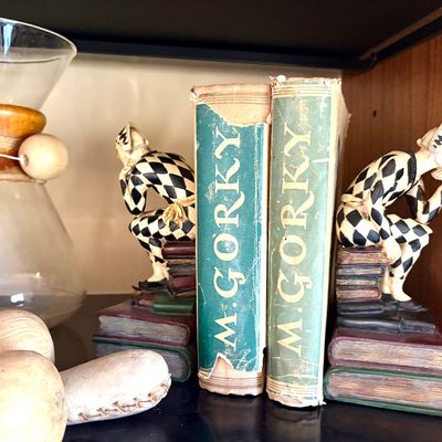 Pair of vintage harlequin bookends depicting a thinking jester seated on a stack of books, shown holding two volumes of Maxim Gorky.