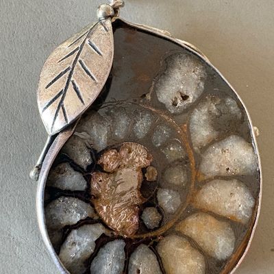 Polished ammonite fossil pendant set in a sterling silver frame with a decorative leaf accent.