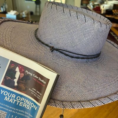 Flying Color Studios woven straw hat in a lavender-grey hue, featuring a flat crown, wide brim with whipstitched edges, and a thin...