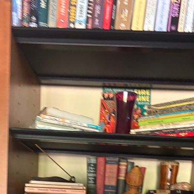 Wooden bookshelf filled with a variety of hardcover and paperback books, interspersed with small decorative items including a purple...