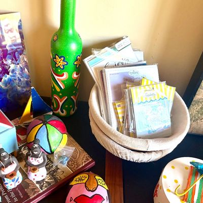 Assortment of colorful decorative items, including a hand-painted green bottle, small clay figurines, a fabric-lined basket filled with...