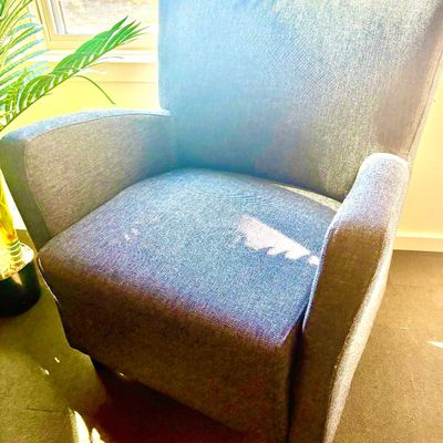 Contemporary upholstered armchair in a textured gray fabric, featuring a high back and curved armrests.