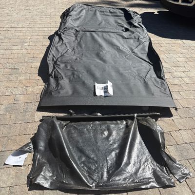 Black vinyl soft top replacement kit for a vehicle, laid out on a paved driveway with instructions included.