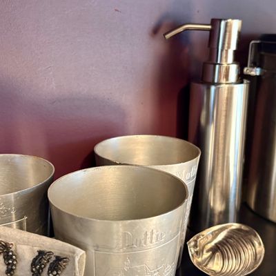 Vintage engraved aluminum cups, including one marked 'Dottie', shown alongside a modern stainless steel soap dispenser and...