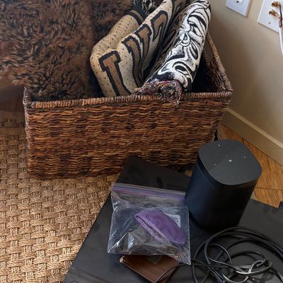 Large woven storage basket containing folded blankets and a faux fur throw, shown alongside a Sonos smart speaker and a Sony electronic...